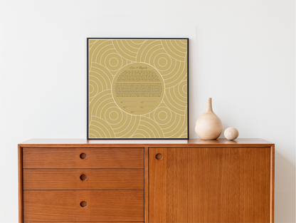 A framed gold and white geometric patterned ketubah artwork displayed on a wooden wall, with a beige vase containing a sprig of greenery to the right.